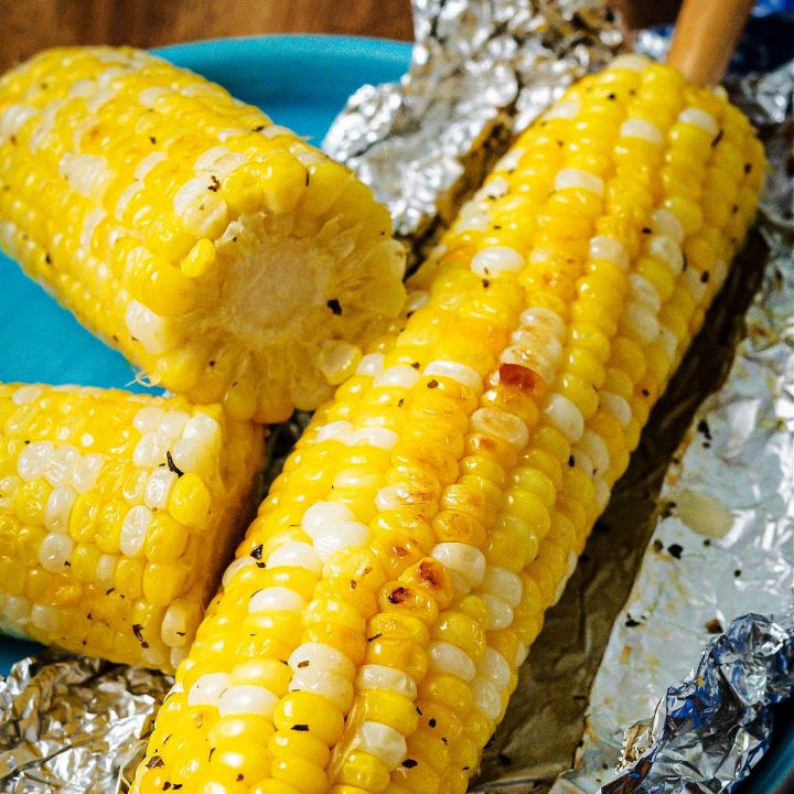 an ear of corn grilled in foil on a plate.