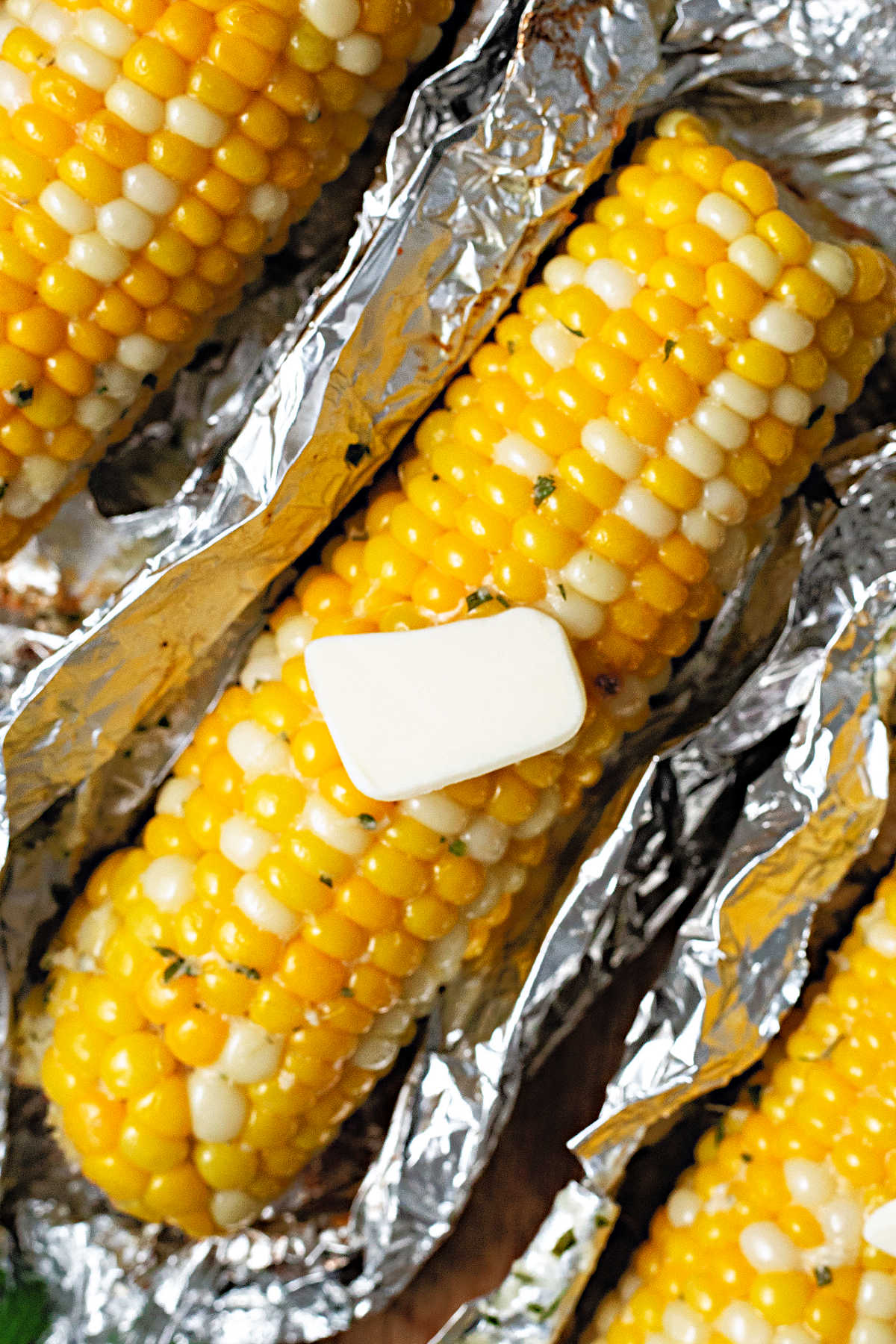 an unwrapped ear of grilled corn in foil with a pat of butter melting on top.