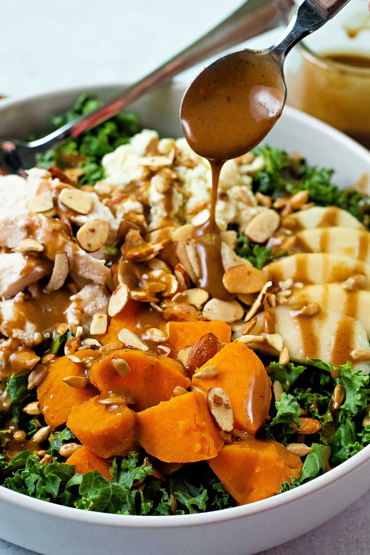 drizzling balsamic dressing from a spoon onto a bowl of salad.