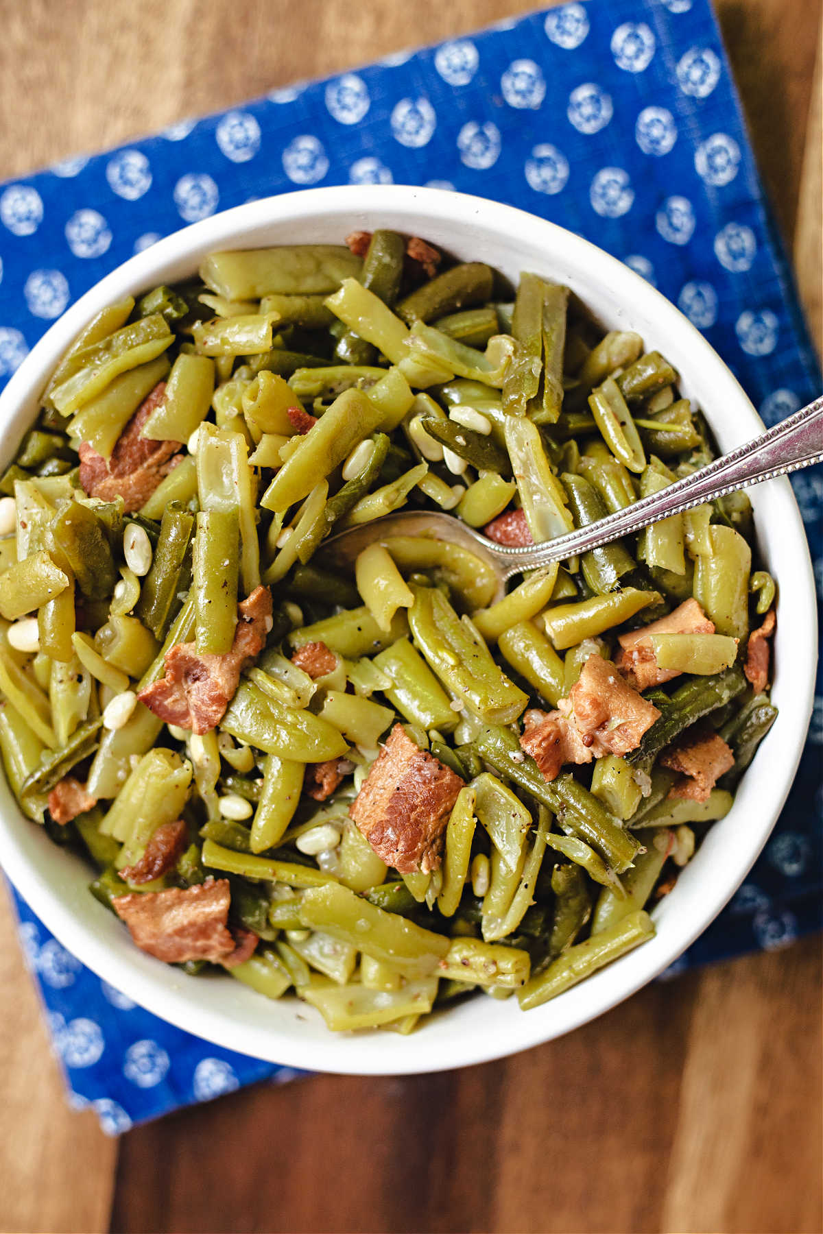 a bowl of green beans with a serving spoon sitting on a blue napkin on a wooden table.
