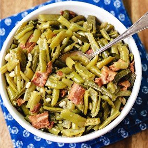 a bowl of green beans with a serving spoon sitting on a blue napkin on a wooden table.