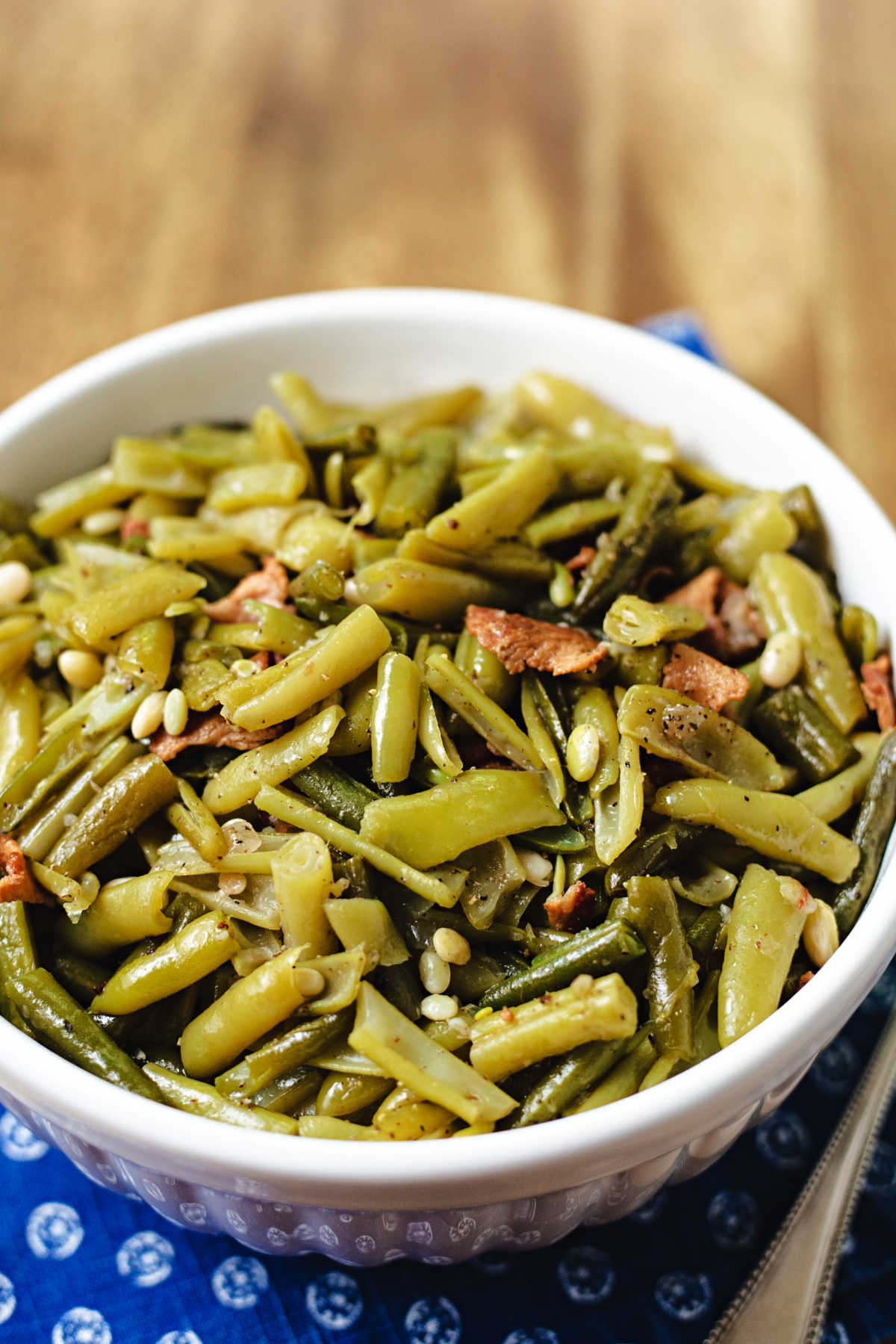 a bowl of green beans sitting on a blue napkin on a wooden table.