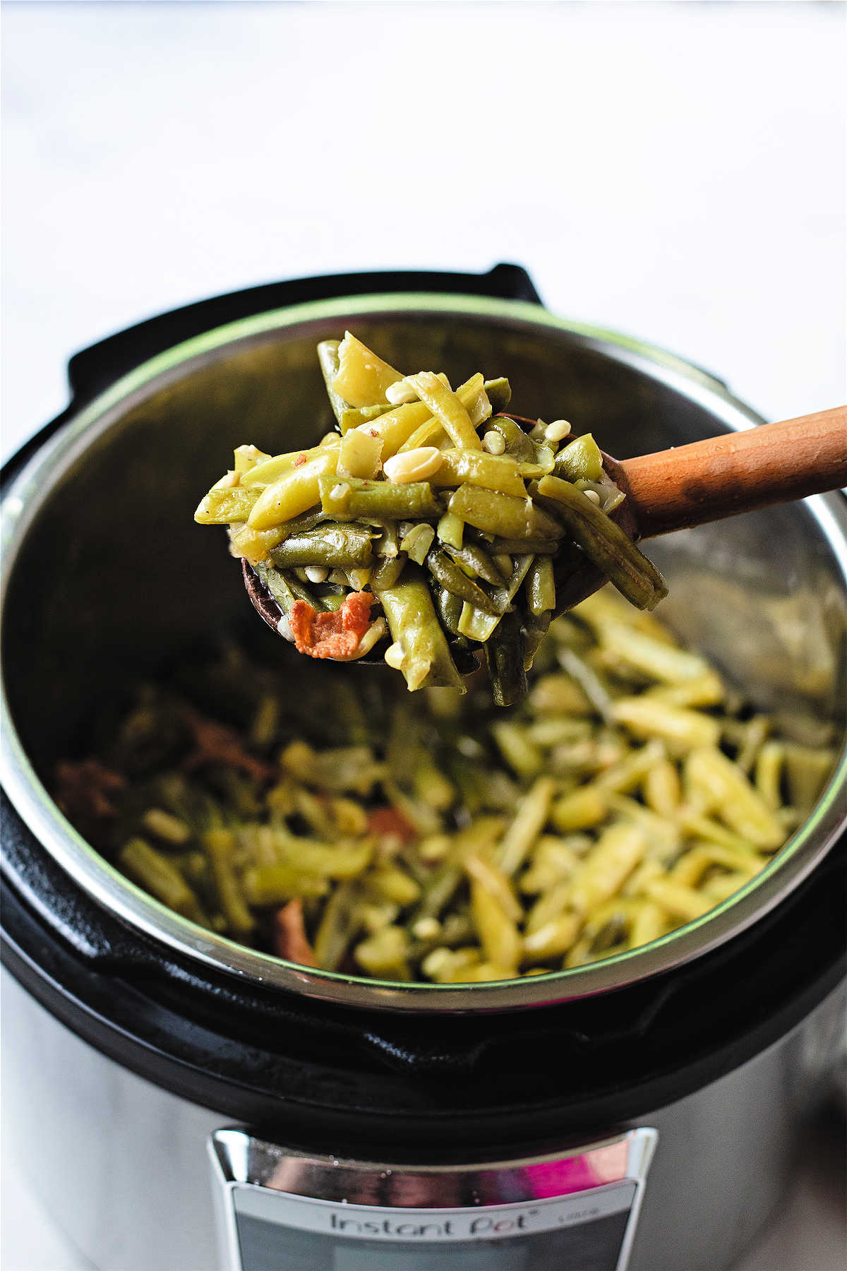 a wooden spoon lifting green beans out of an instant pot.