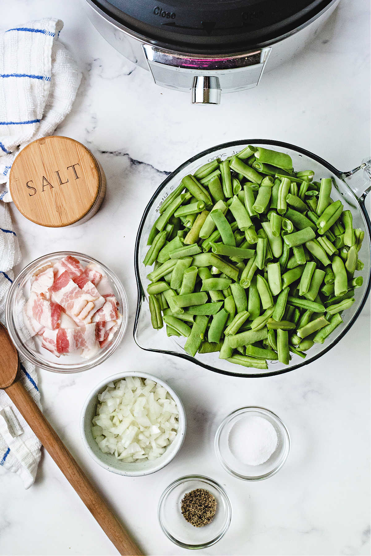 ingredients for cooking green beans in an instant pot on a kitchen counter: fresh green beans, bacon, diced onion, salt, pepper, and sugar.