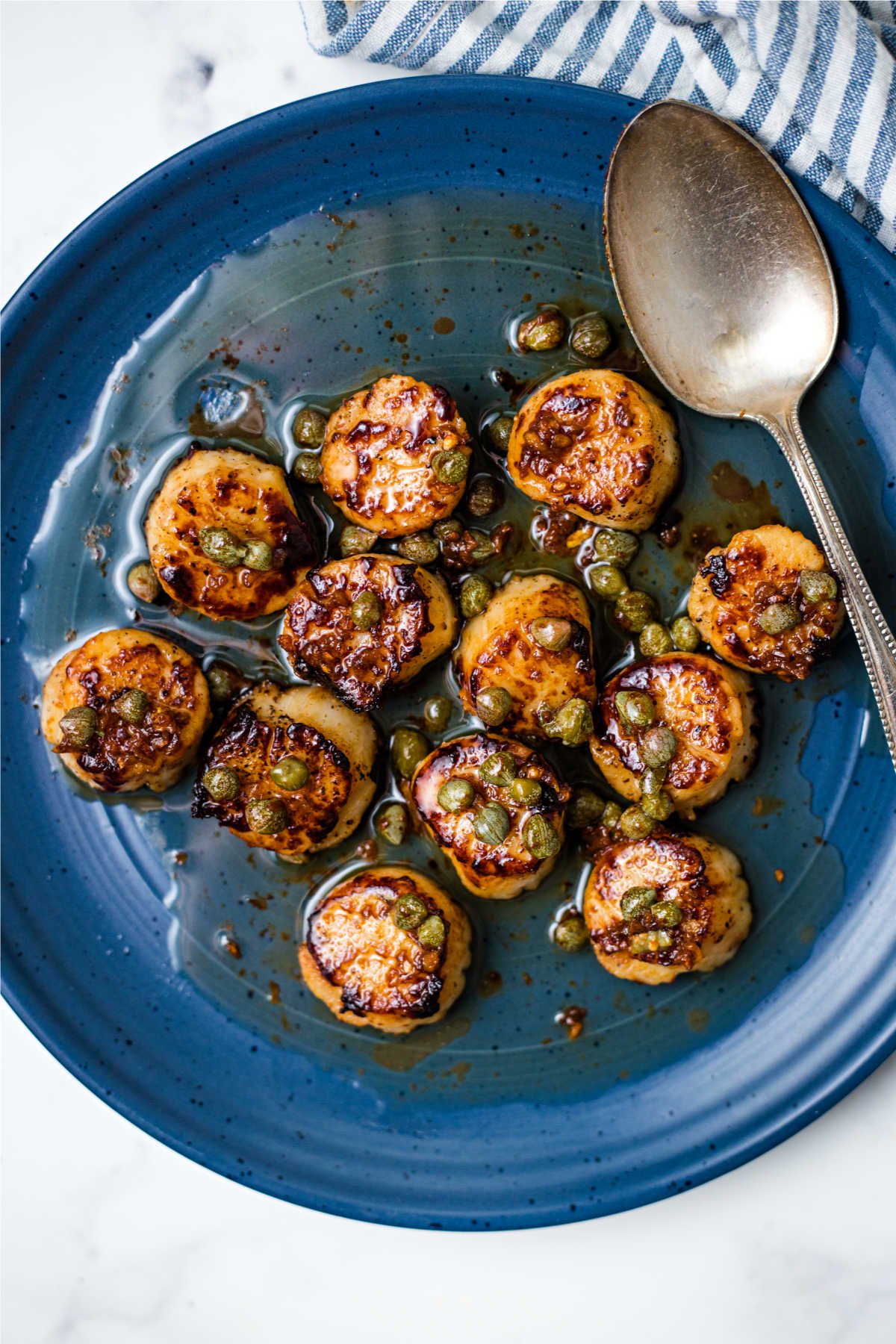 seared scallops with brown butter sauce on a blue plate with capers.