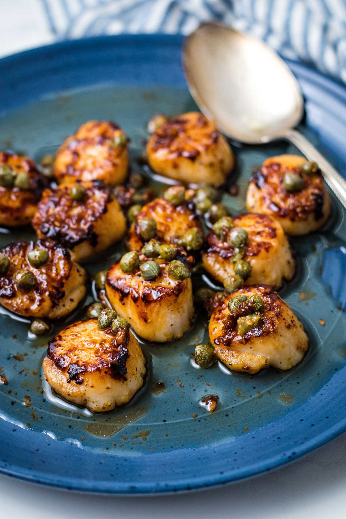 seared scallops with brown butter sauce on a blue plate with capers.