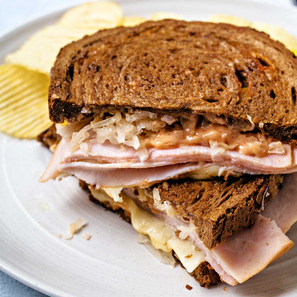 a turkey reuben sandwich cut in half and stacked on top of each other on a white plate with potato chips.