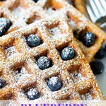 blueberry waffles stacked on top of each other and dusted with powdered sugar and sprinkled with blueberries.