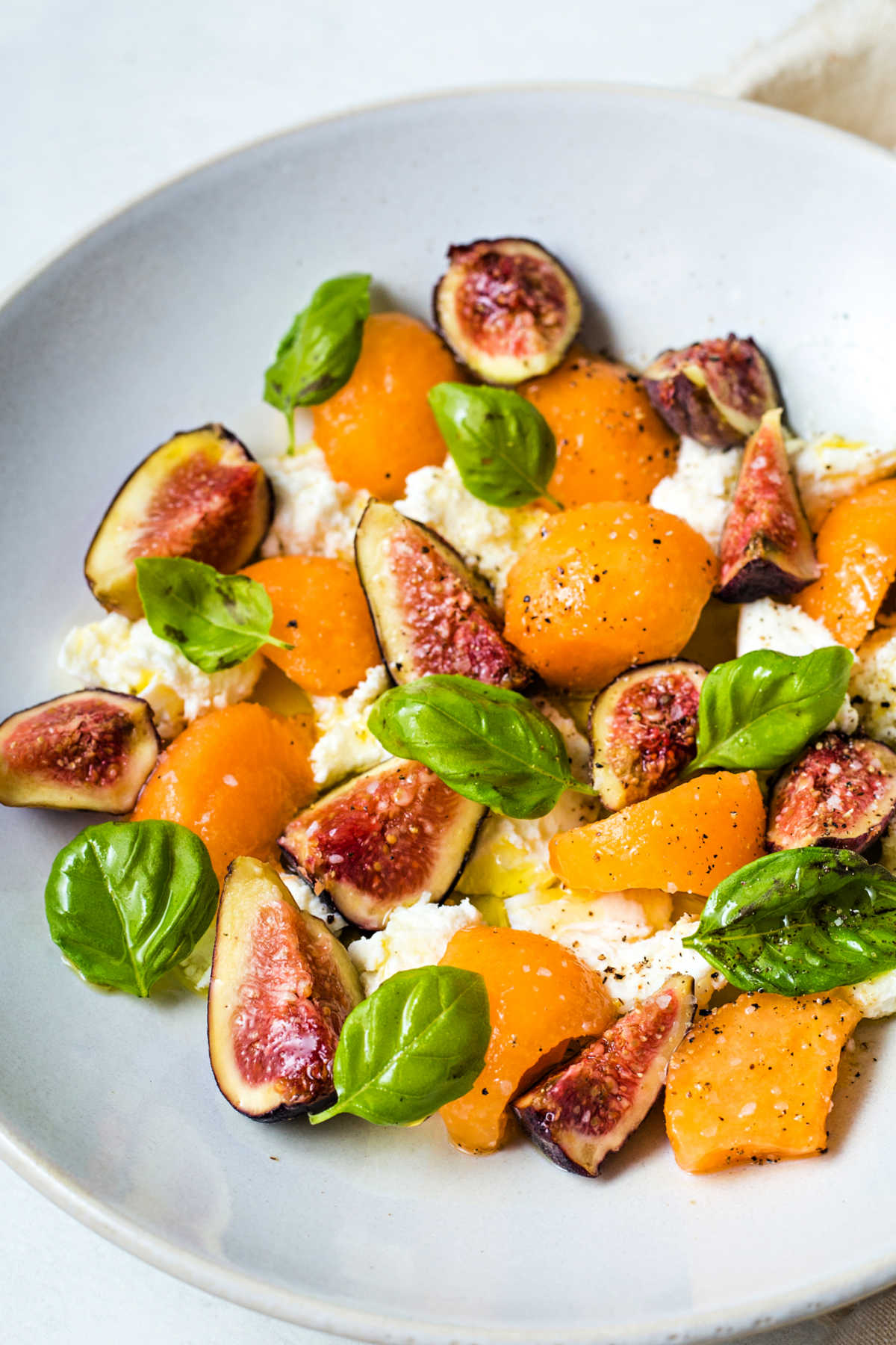 fig salad with fresh mozzarella and cantaloupe in a shallow white bowl on a table.