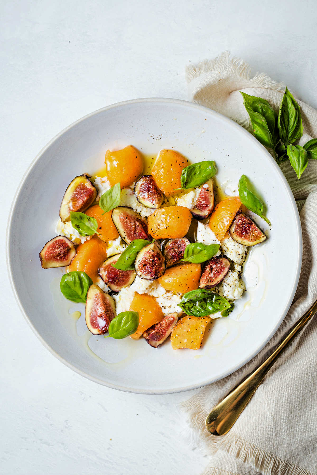 fig salad with fresh mozzarella and cantaloupe in a shallow white bowl on a table.