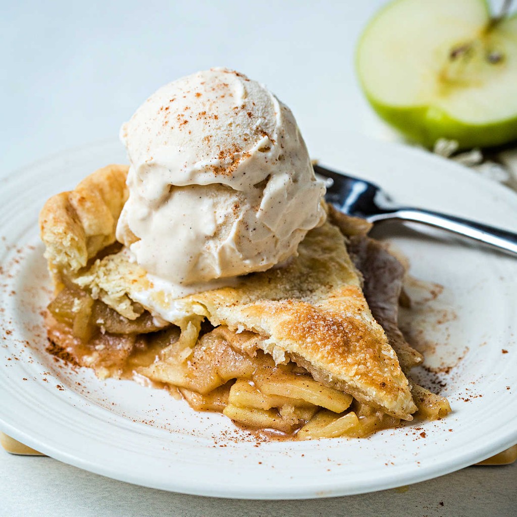 a slice of apple pie on a white plate with a scoop of vanilla ice cream and sprinkled with cinnamon.