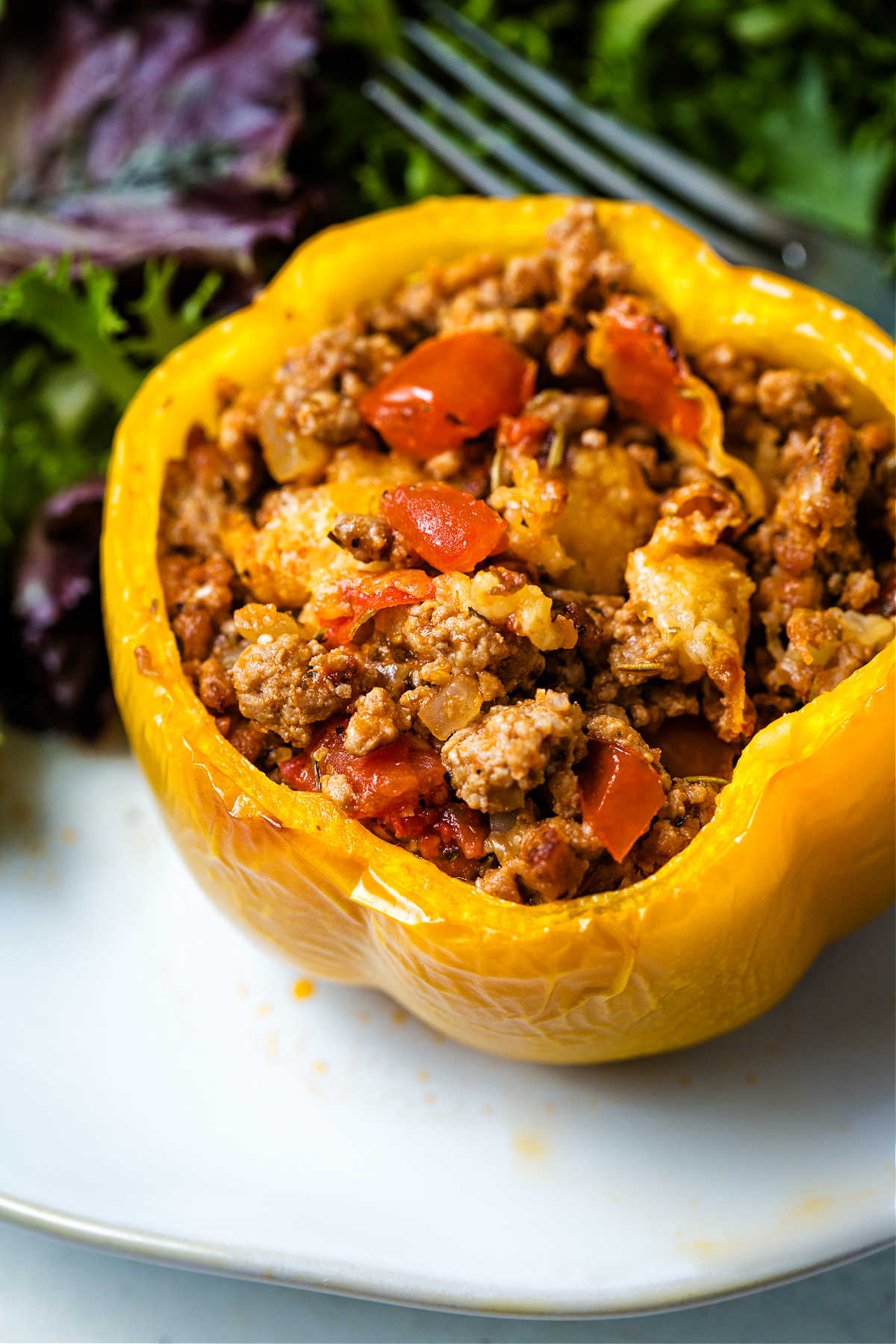 a yellow bell pepper stuffed with saucy turkey mixture on a plate with a side salad.