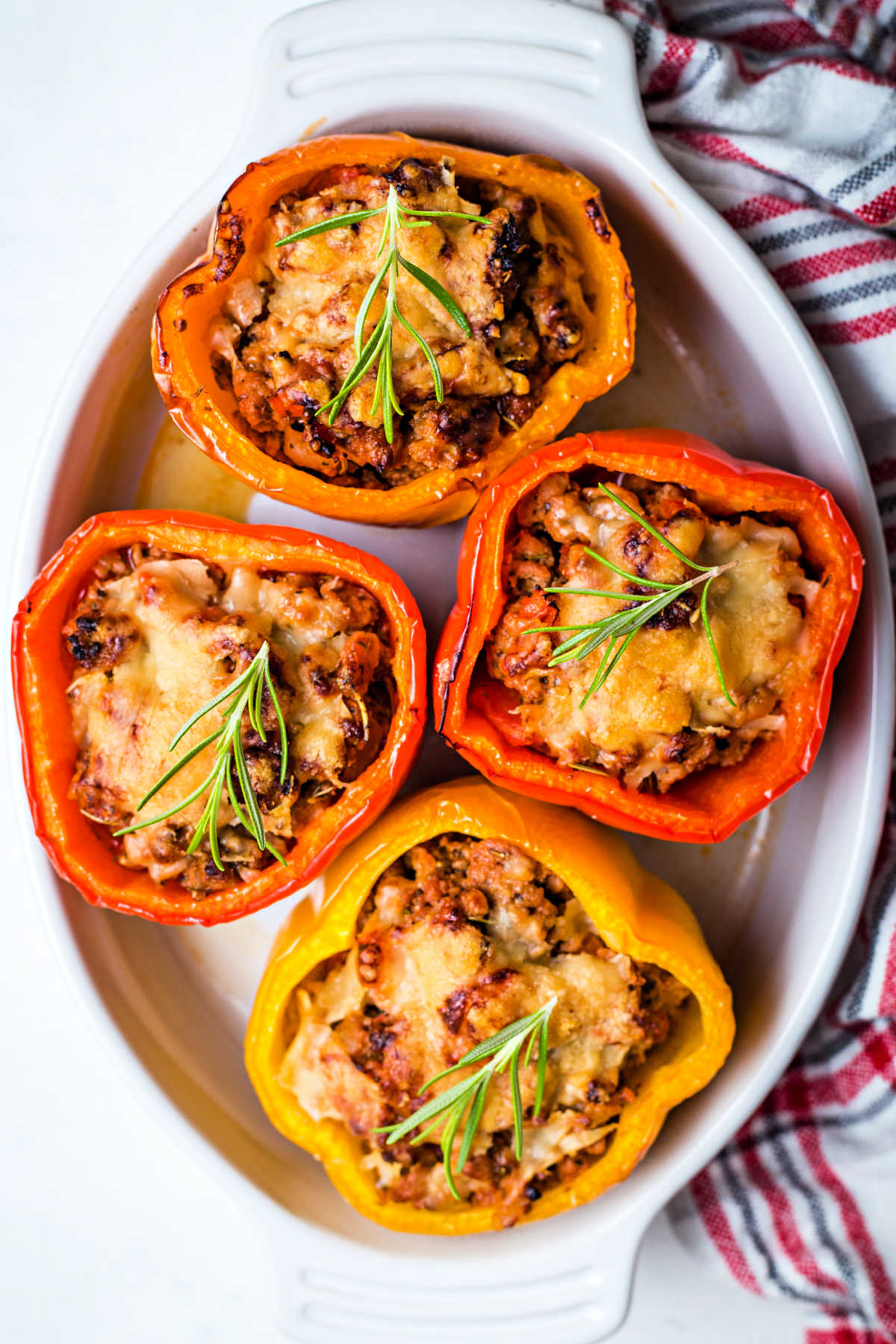 four saucy turkey stuffed peppers in a white baking dish on a table.