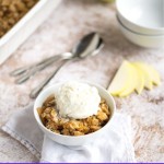 EASY APPLE CRISP IN A WHITE BOWL WITH A SCOOP OF VANILLA ICE CREAM ON A TABLE.