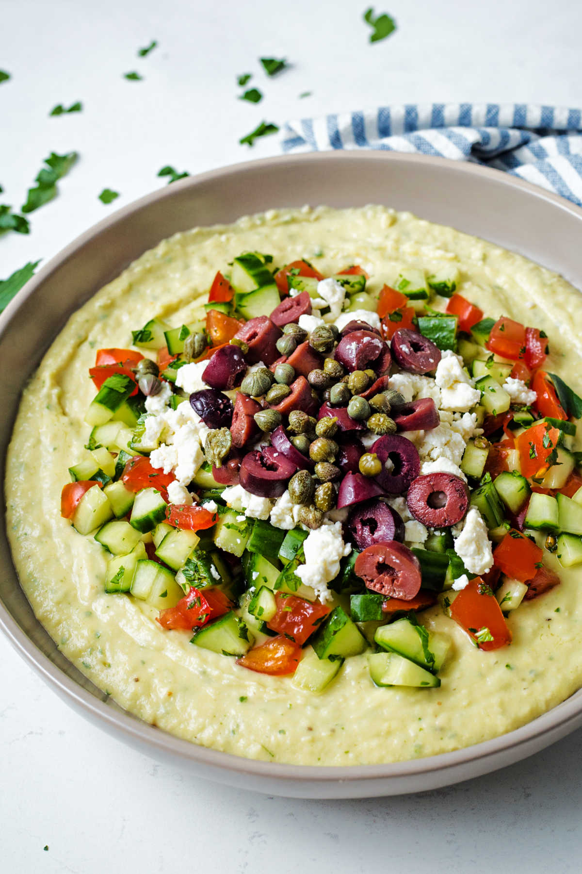 close up view of a bowl of layered greek hummus dip with feta cheese and olives.