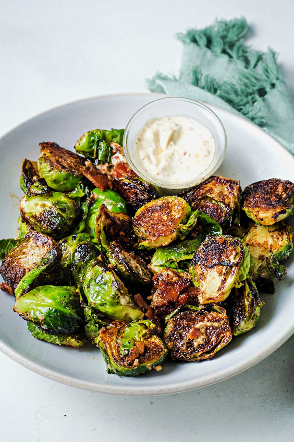 caramelized brussels sprouts in a white serving bowl with a a side of garlic aioli on a table.