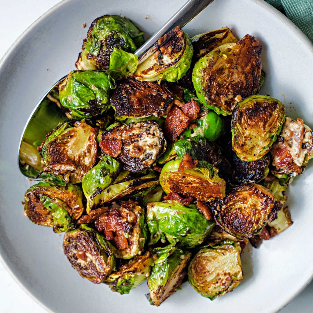 caramelized brussels sprouts in a white serving bowl with a spoon on a table.
