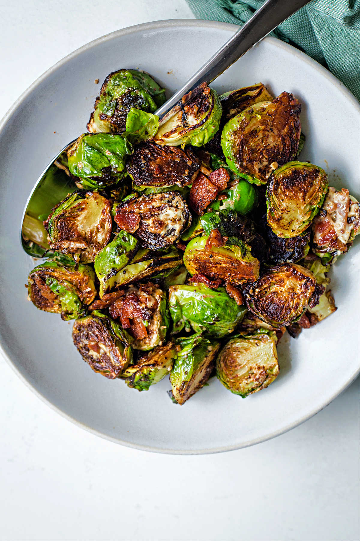 caramelized brussels sprouts in a white serving bowl with a spoon on a table.