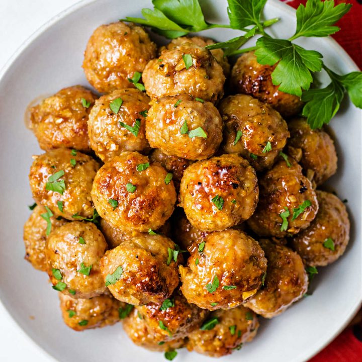 close up of a plate of chicken meatballs garnished with parsley on top of a red napkin on a table.