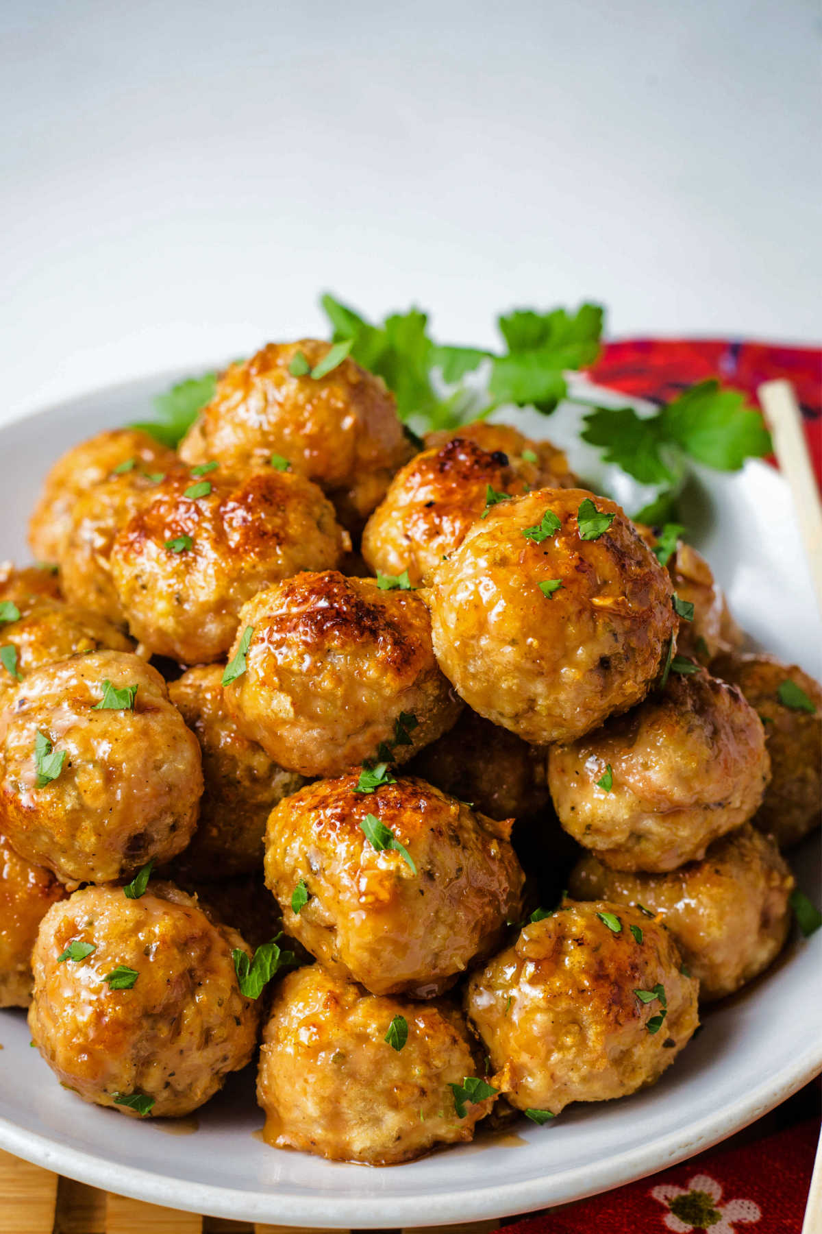 side view of a plate of chicken meatballs garnished with parsley on top of a red napkin on a table.