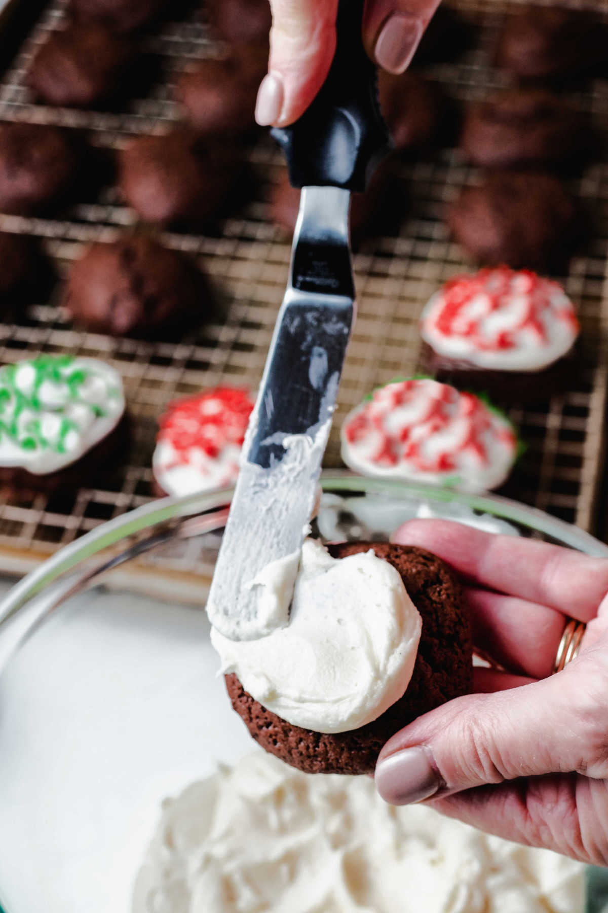 using a spatula to spread frosting on a chocolate drop cookie.