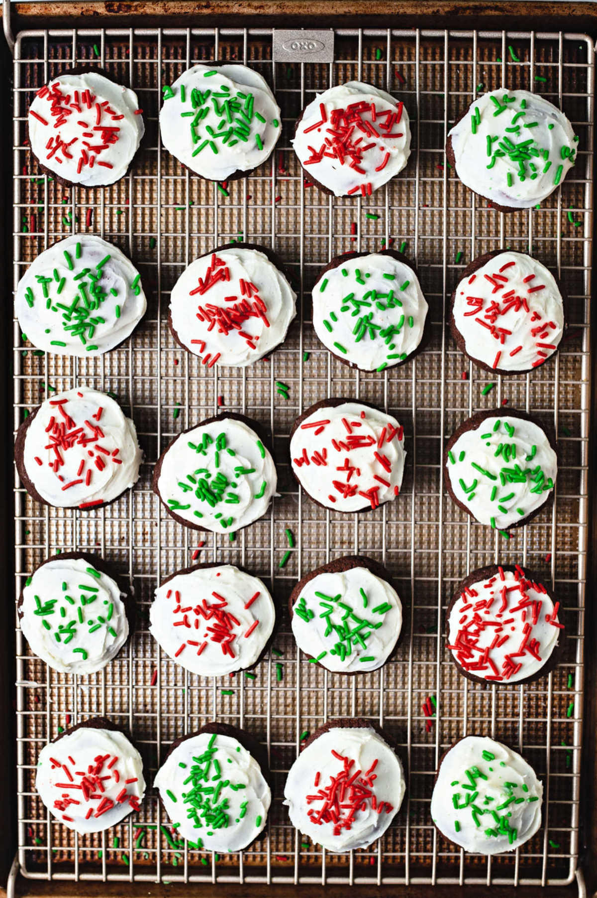 chocolate drop cookies with vanilla frosting and red and green sprinkles on a wire cooling rack.
