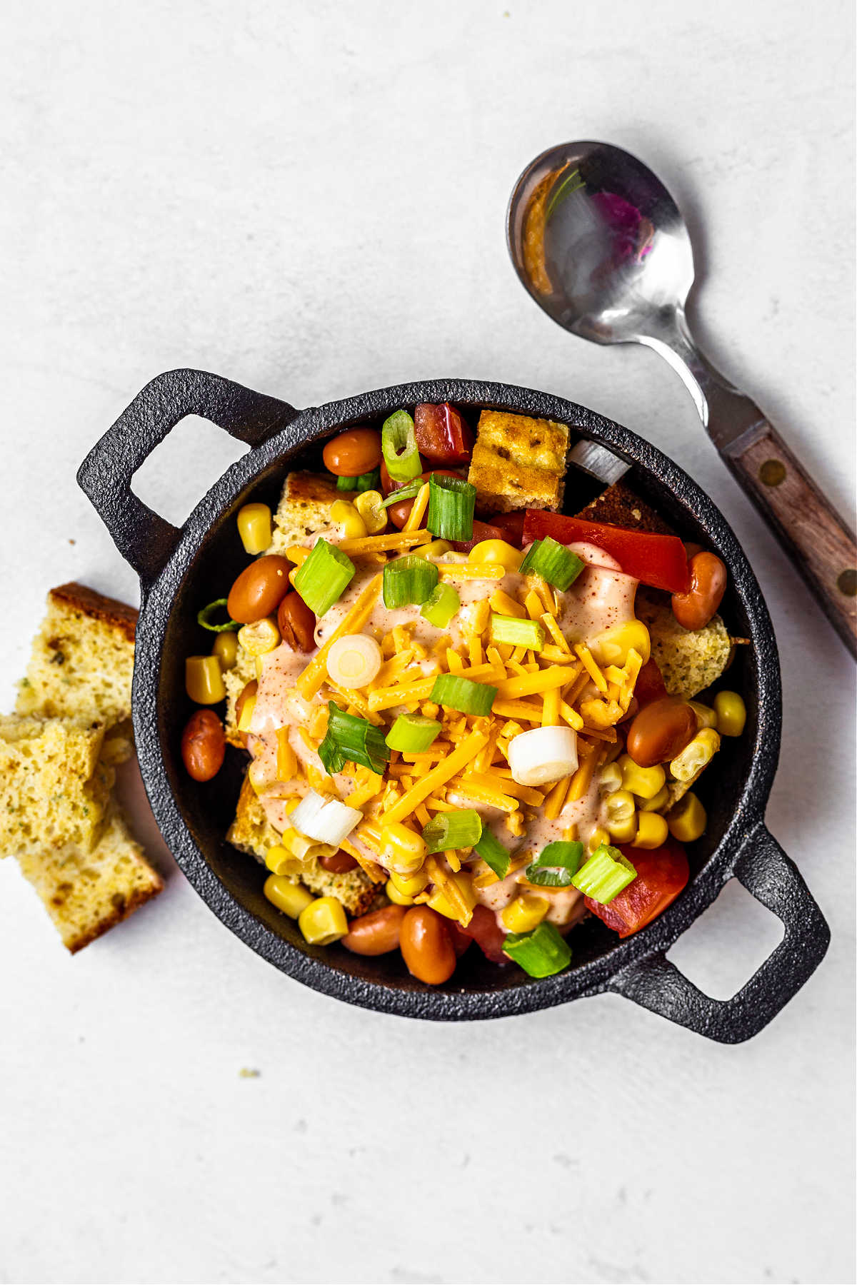 a serving of cornbread salad in a mini cast iron skilled with a spoon and yellow napkin on a table.