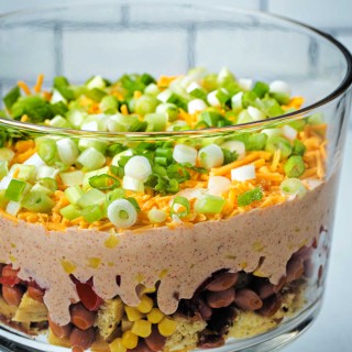 seven layer cornbread salad in a glass trifle bowl on a kitchen counter.