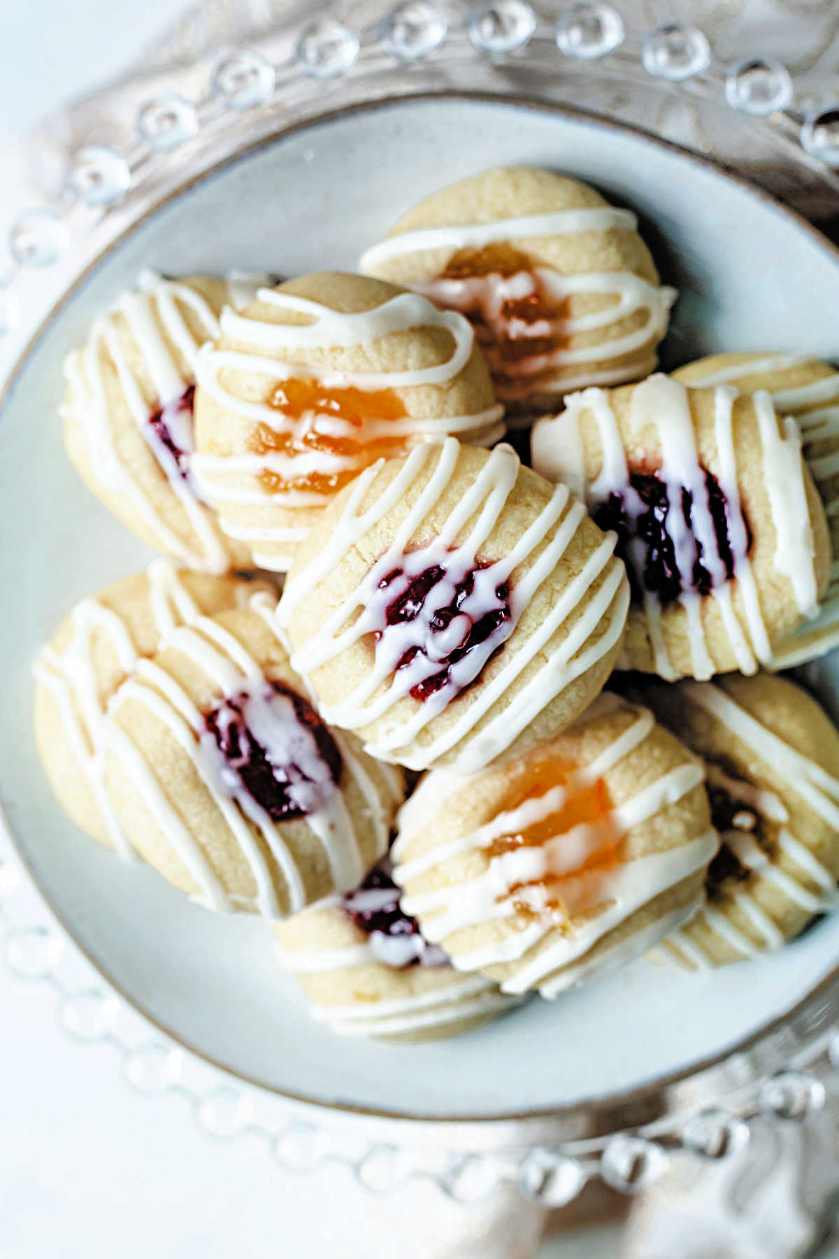 top down view of a plate of jam thumbprint lemon short bread cookies with raspberry and orange marmalade filling sitting on a cake stand..