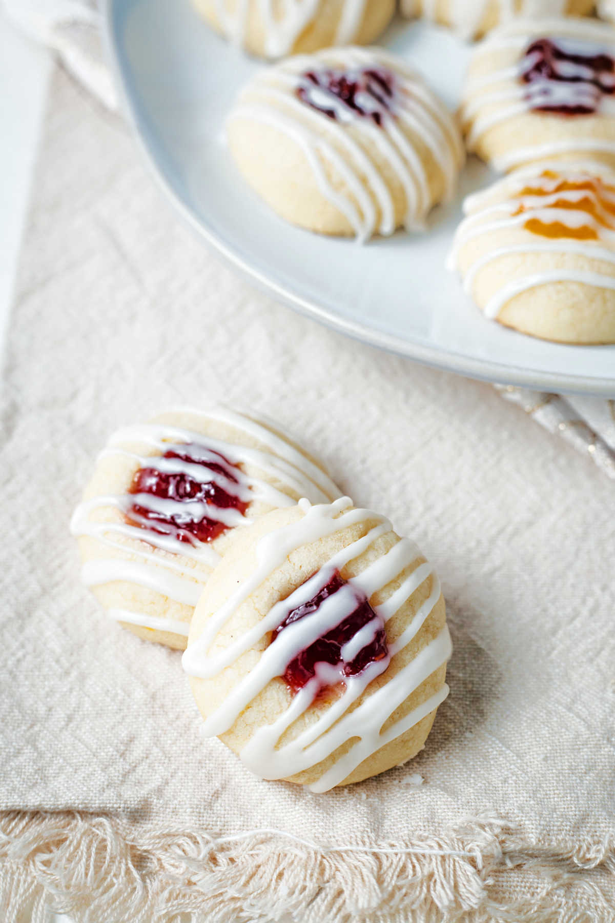 two raspberry jam filled thumbprint lemon shortbread cookies on a linen napkin.