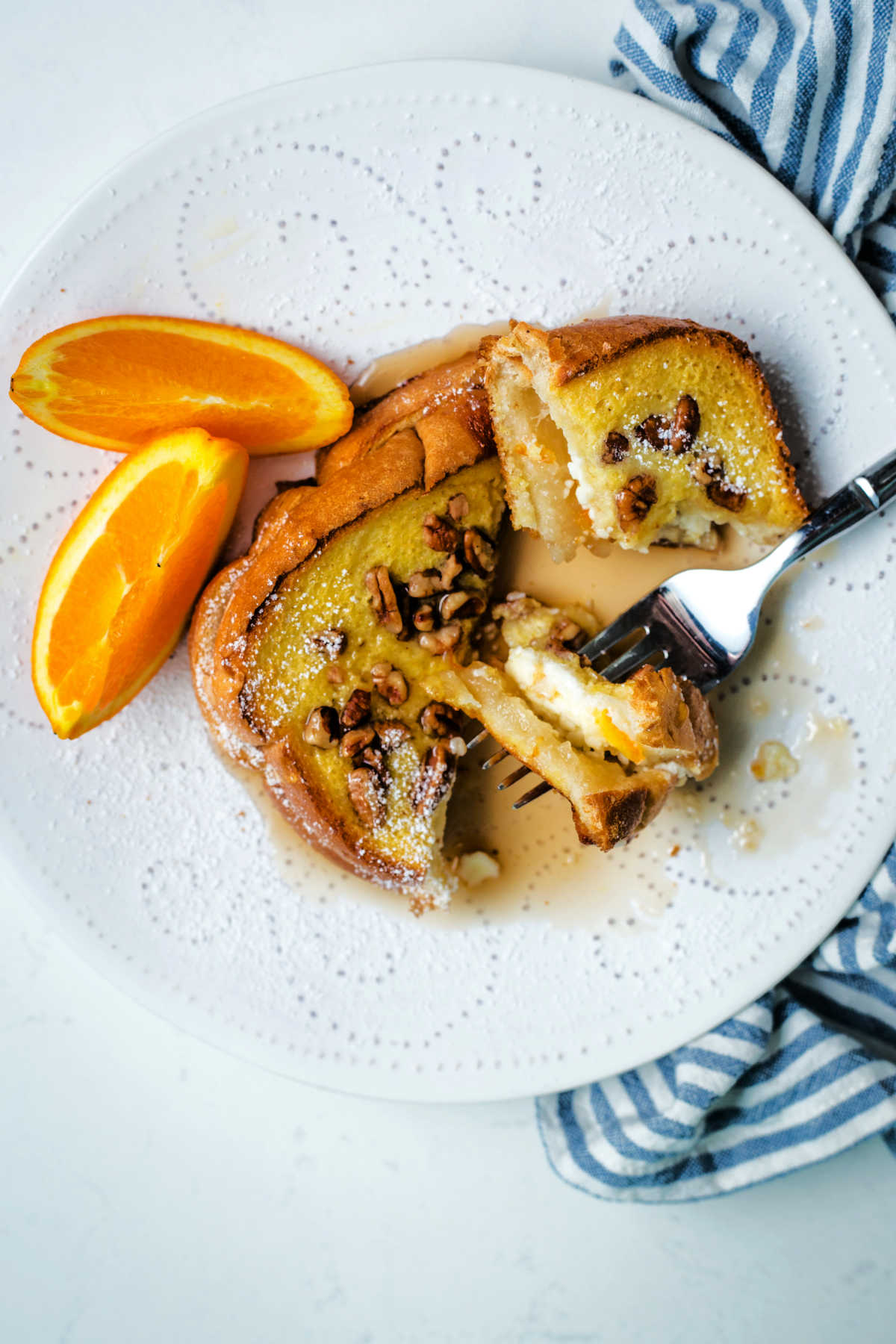 a bite of orange french toast drenched in maple syrup on a fork.