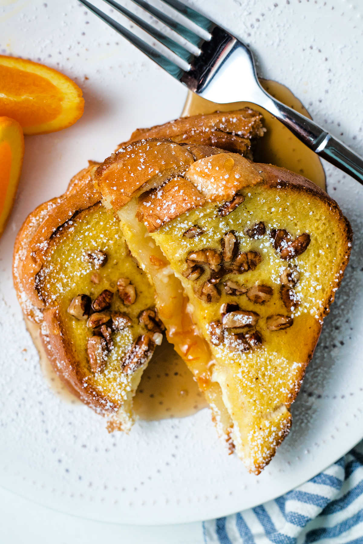 close up shot of two slices of orange french toast with maple syrup oozing onto the plate.