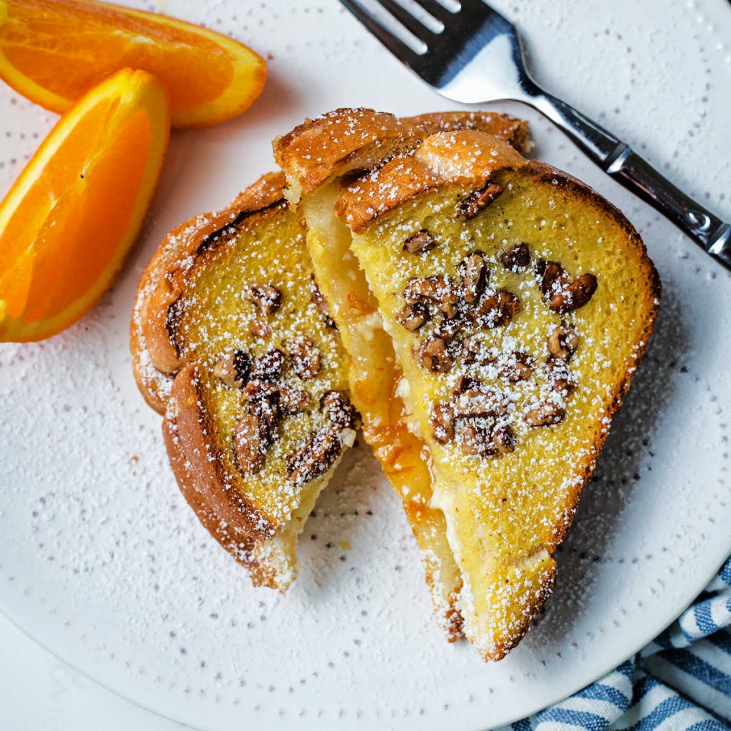 slices of orange french toast on a white plate with orange slices and sprinkled with powdered sugar.