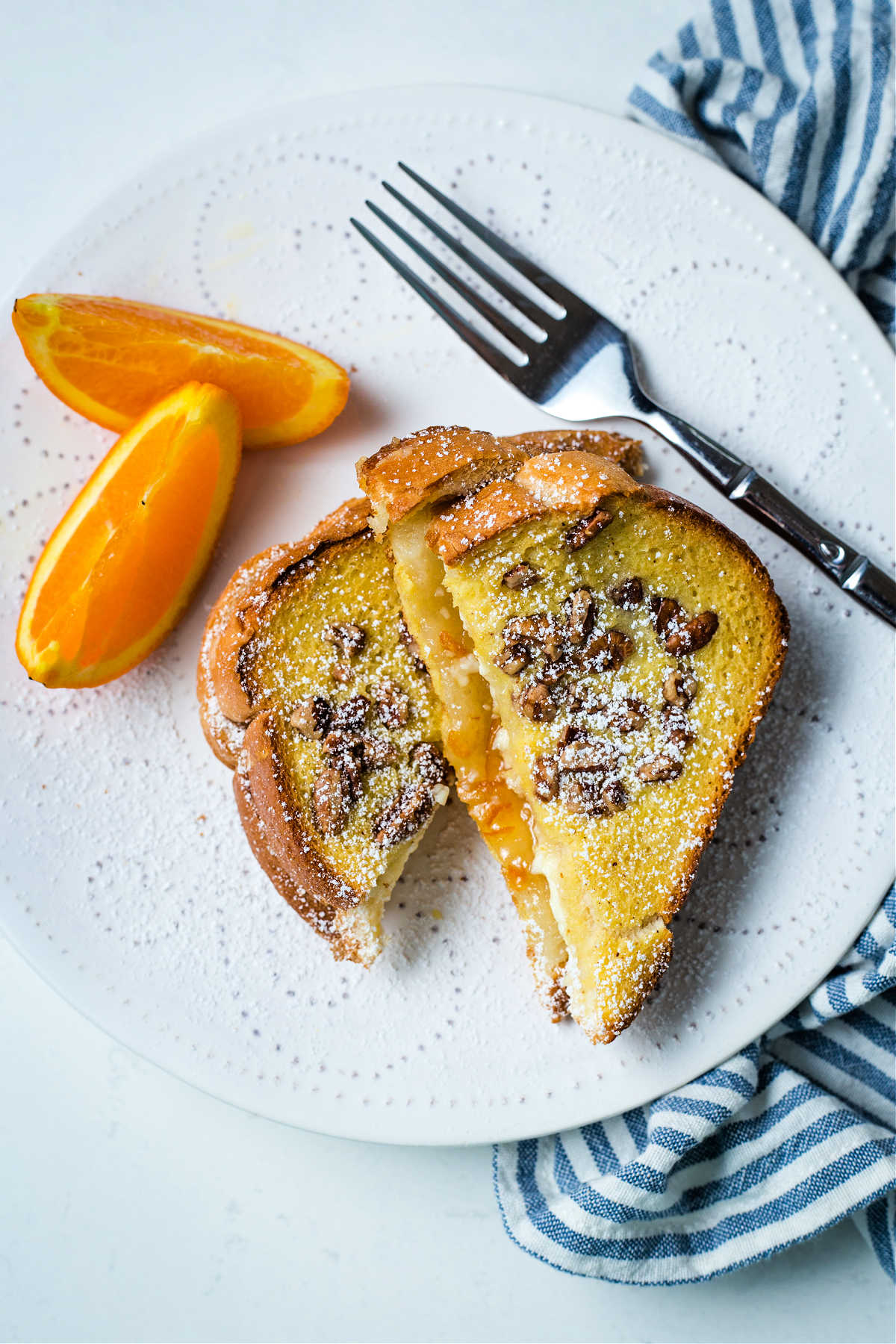 two slices of orange french toast with orange slice garnish on a white plate with a blue napkin and fork.