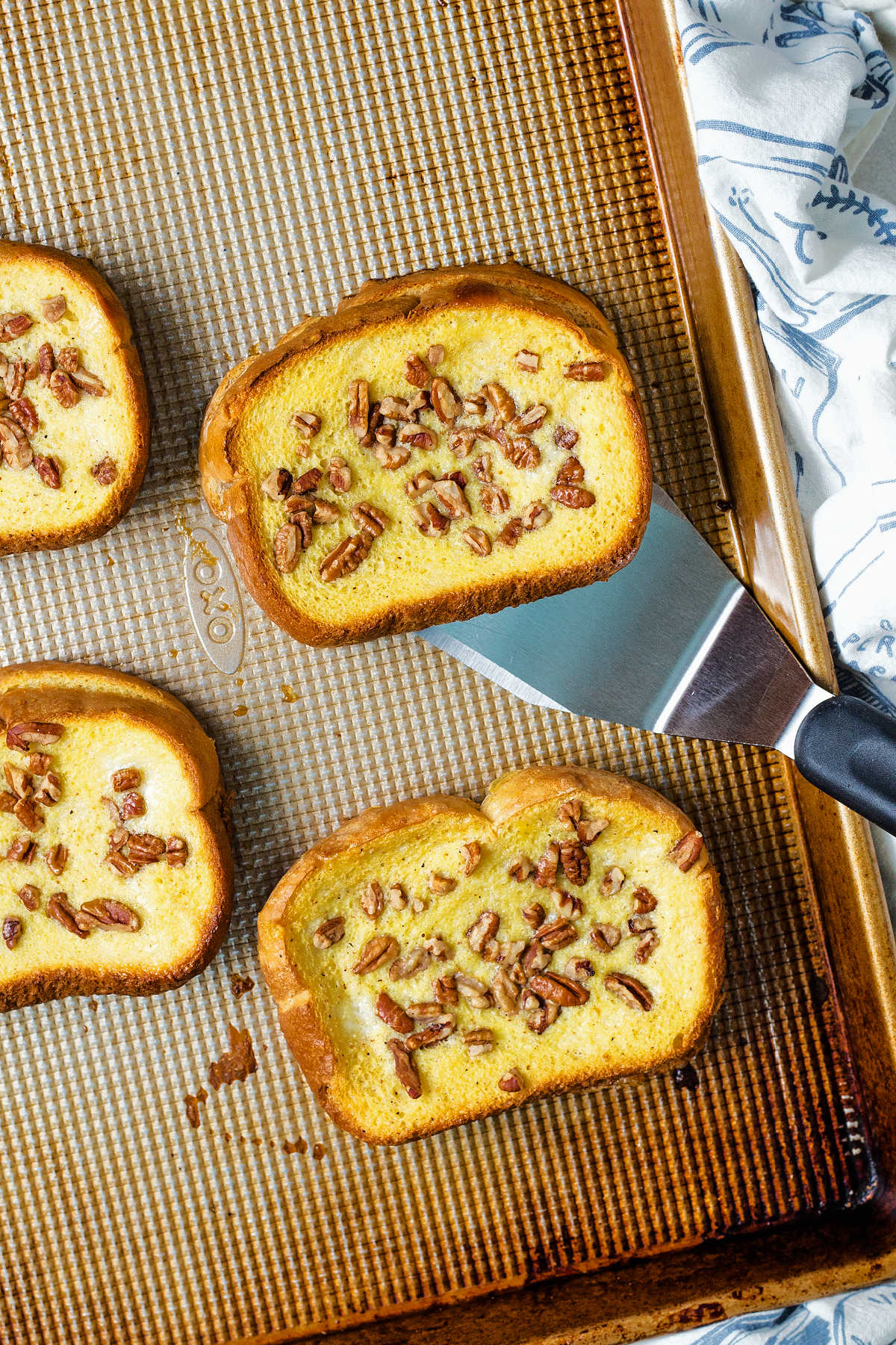 a spatula lifting a piece of orange french toast off of a baking sheet.