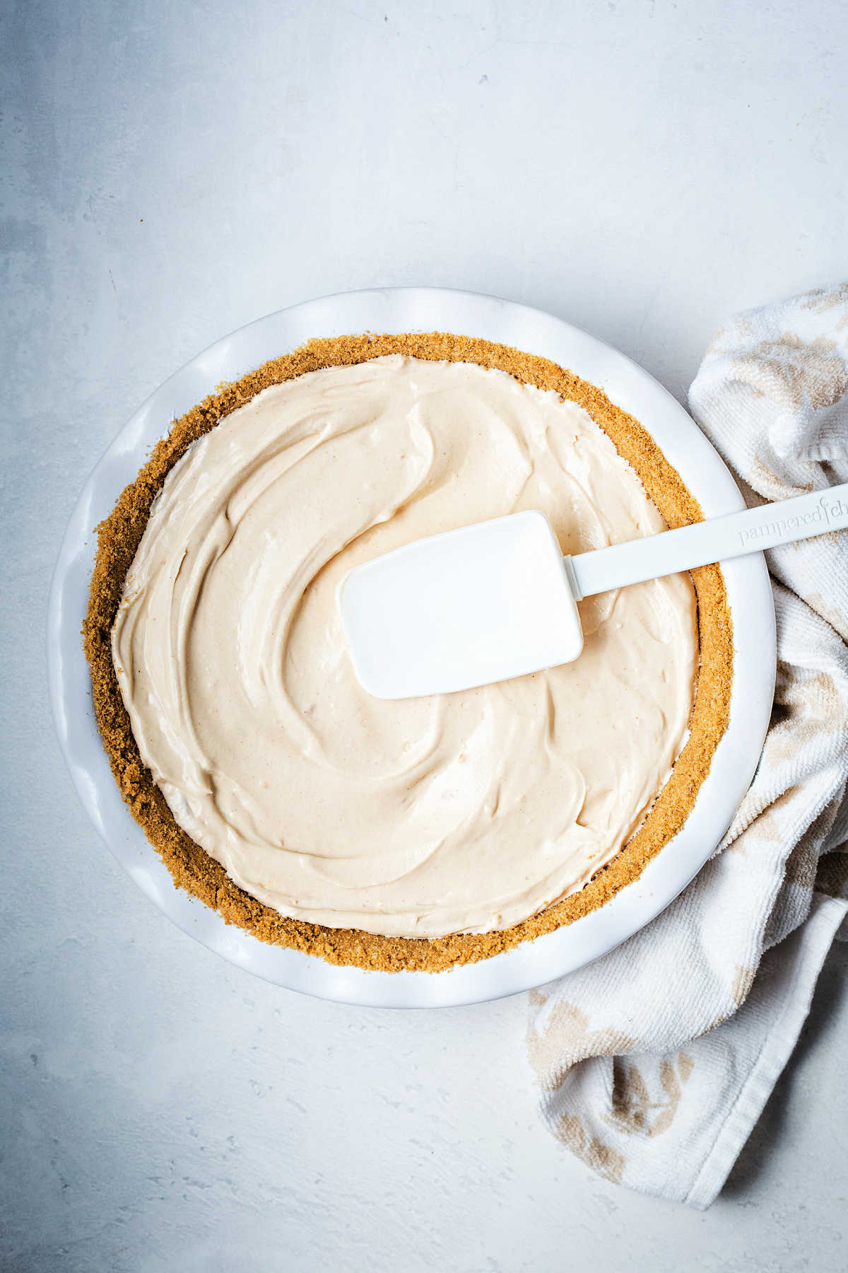 smoothing peanut butter pie filling into a graham cracker crust with a rubber spatula.