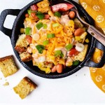 a serving of cornbread salad in a mini cast iron skilled with a spoon and yellow napkin on a table.