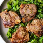 broiled lamb chops on a bed of arugula on a plate.