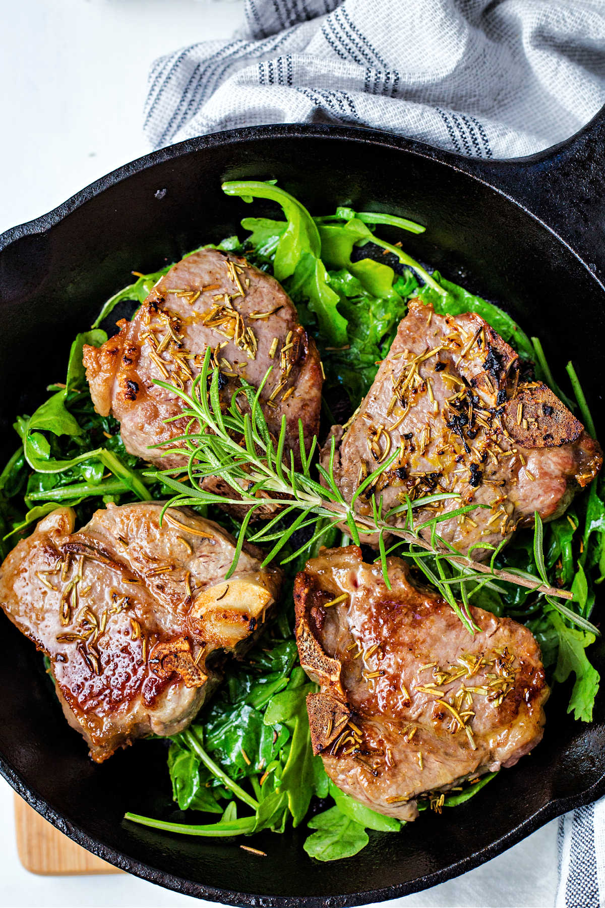broiled lamb chops on a bed of arugula in a cast iron pan and garnished with a sprig of rosemary.