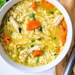 a bowl of lemon chicken orzo soup on a table with parsley and lemon.