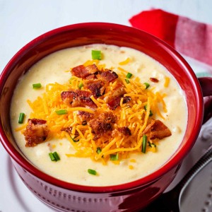 loaded potato soup in a red soup bowl garnished with cheese, bacon, and chives.