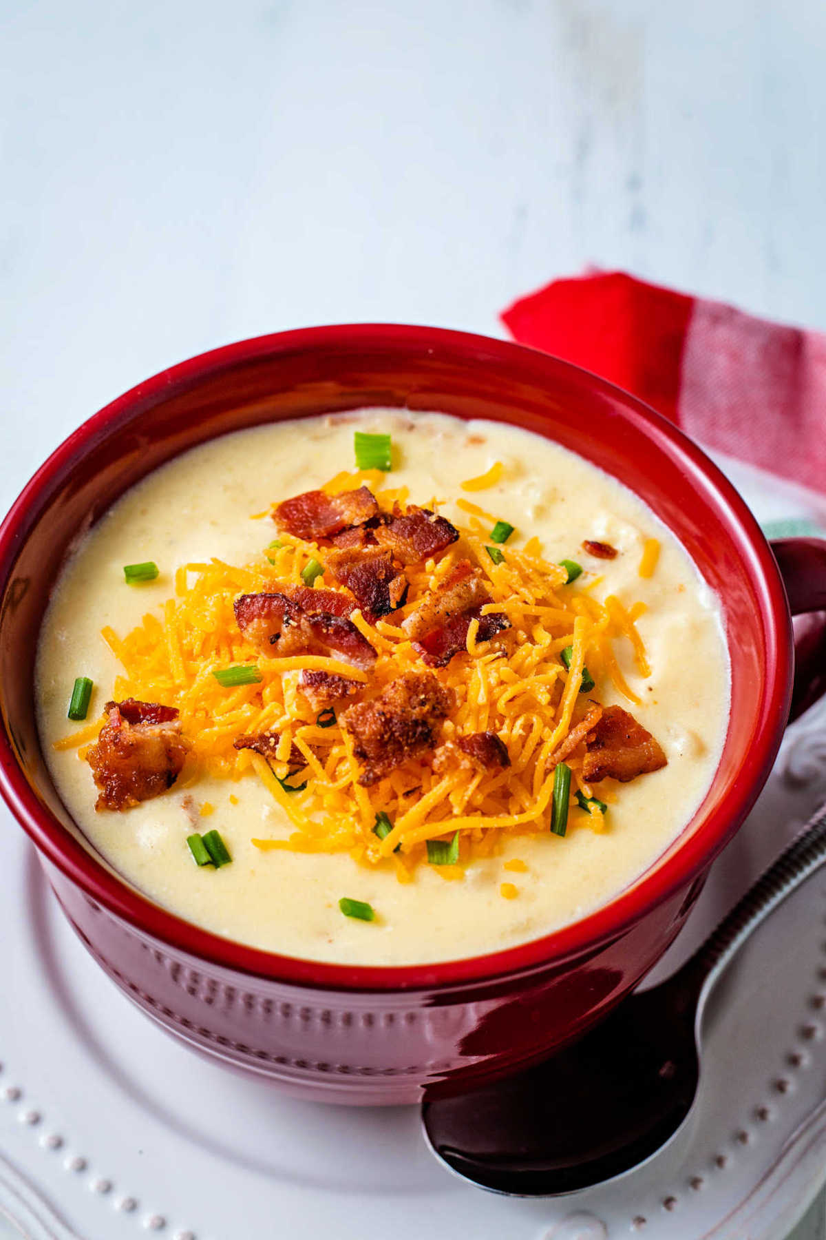 loaded potato soup in a red soup bowl garnished with cheese, bacon, and chives.