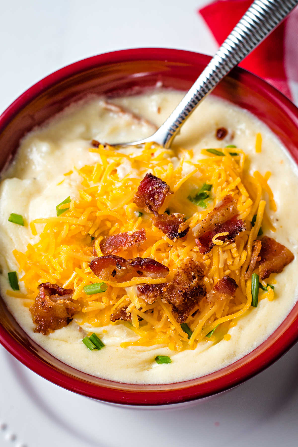 a spoon dipped into a bowl of loaded potato soup sitting on a plate.