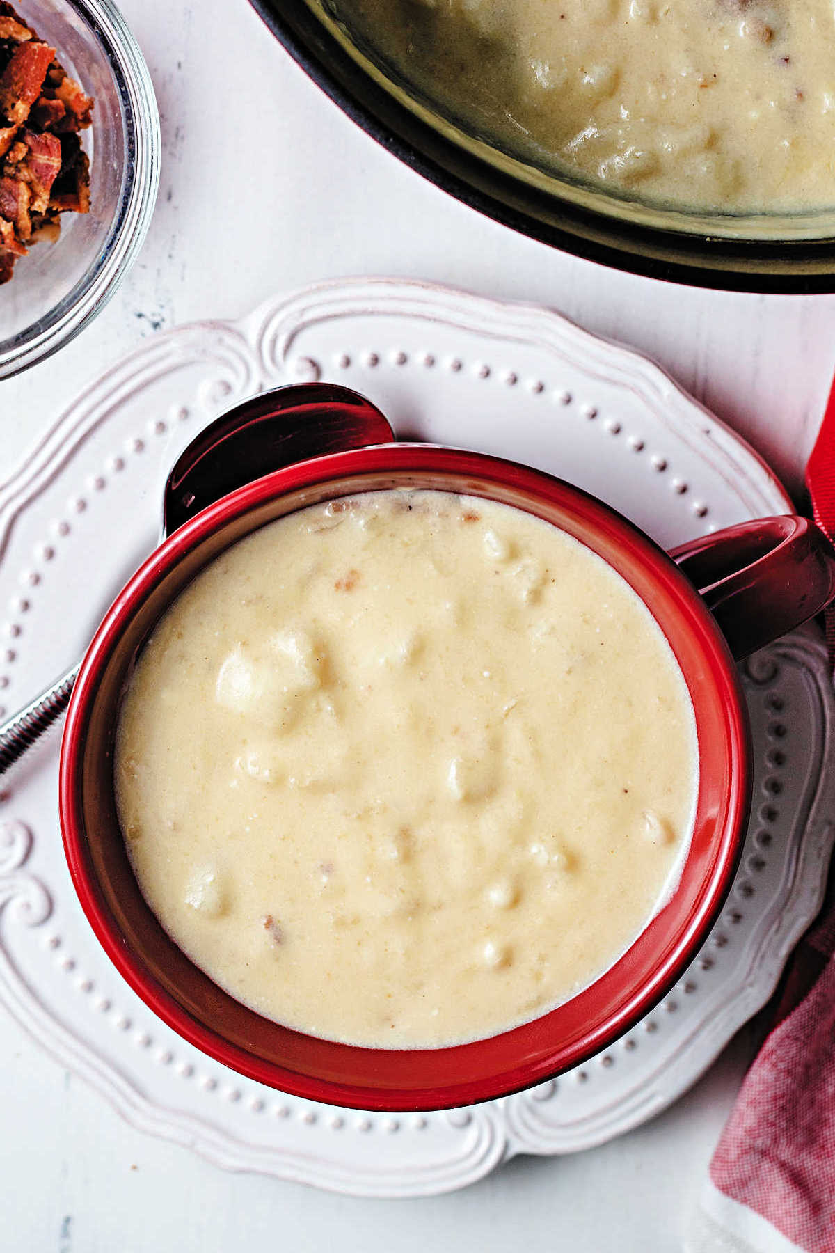 a bowl of loaded potato soup sitting on a white plate with the pot of soup in the background.