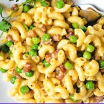 macaroni carbonara with prosciutto and green peas in a white bowl with a parsley garnish.