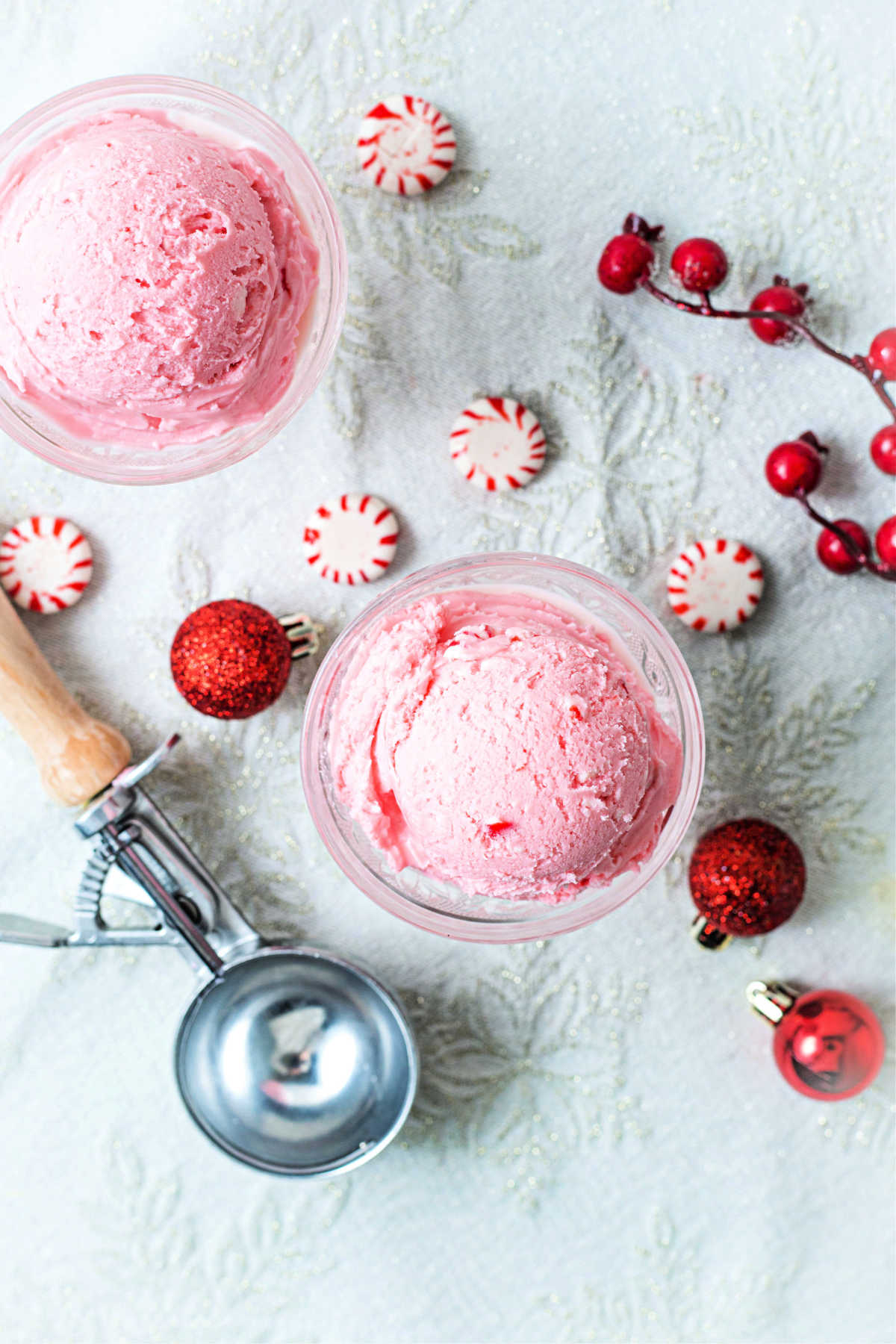 top down view of scoops of peppermint ice cream in two vintage cut glass ice cream bowls on a table with peppermints and an ice cream scoop.
