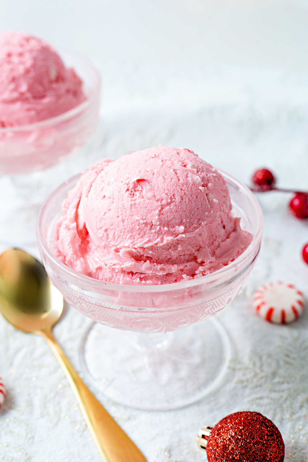 peppermint ice cream in a vintage cut glass ice cream  bowl on a table with peppermints and a gold spoon.