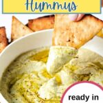 Dipping a pita chip into White Bean Hummus in a bowl.