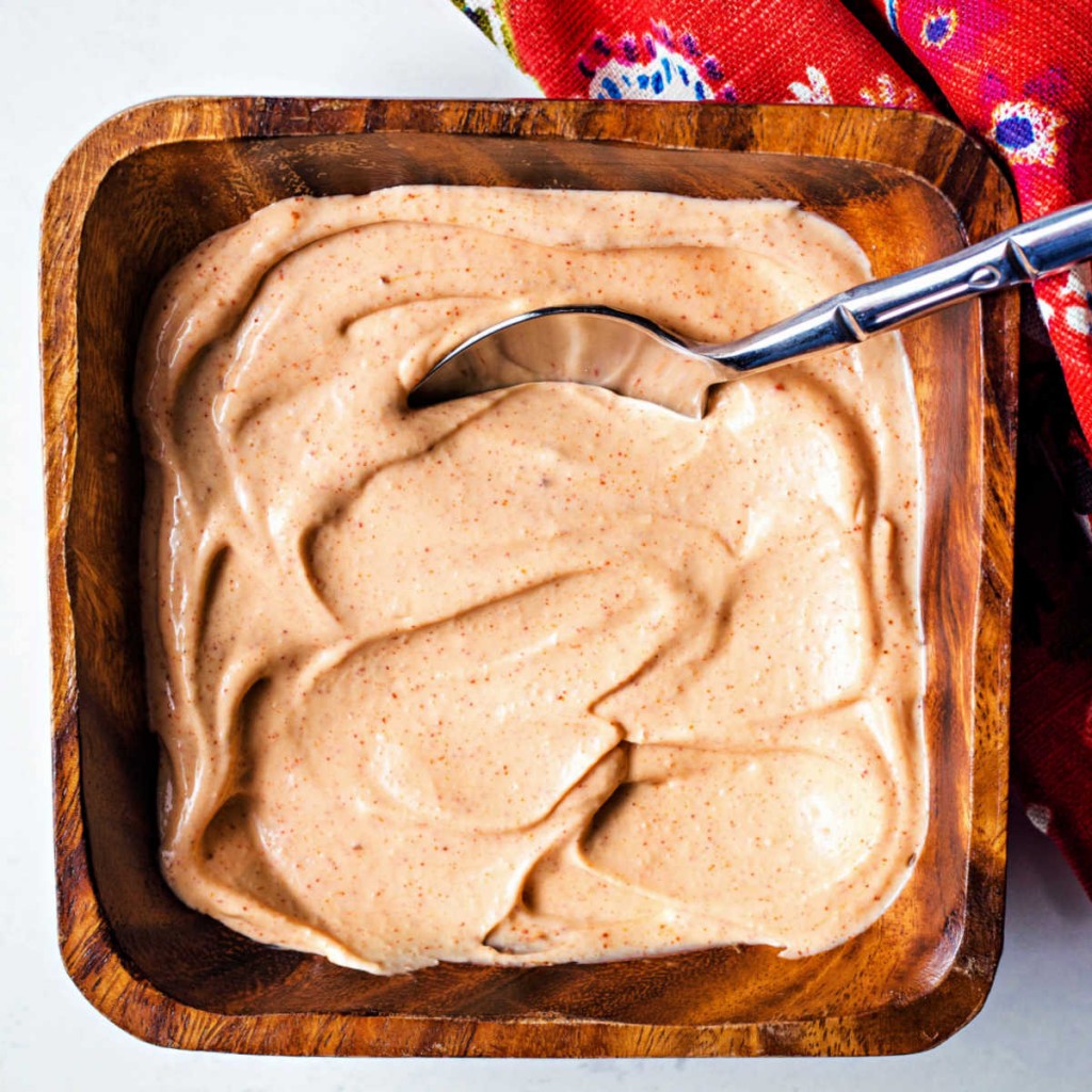 a wooden bowl filled with yum yum sauce with a spoon inserted into the middle.