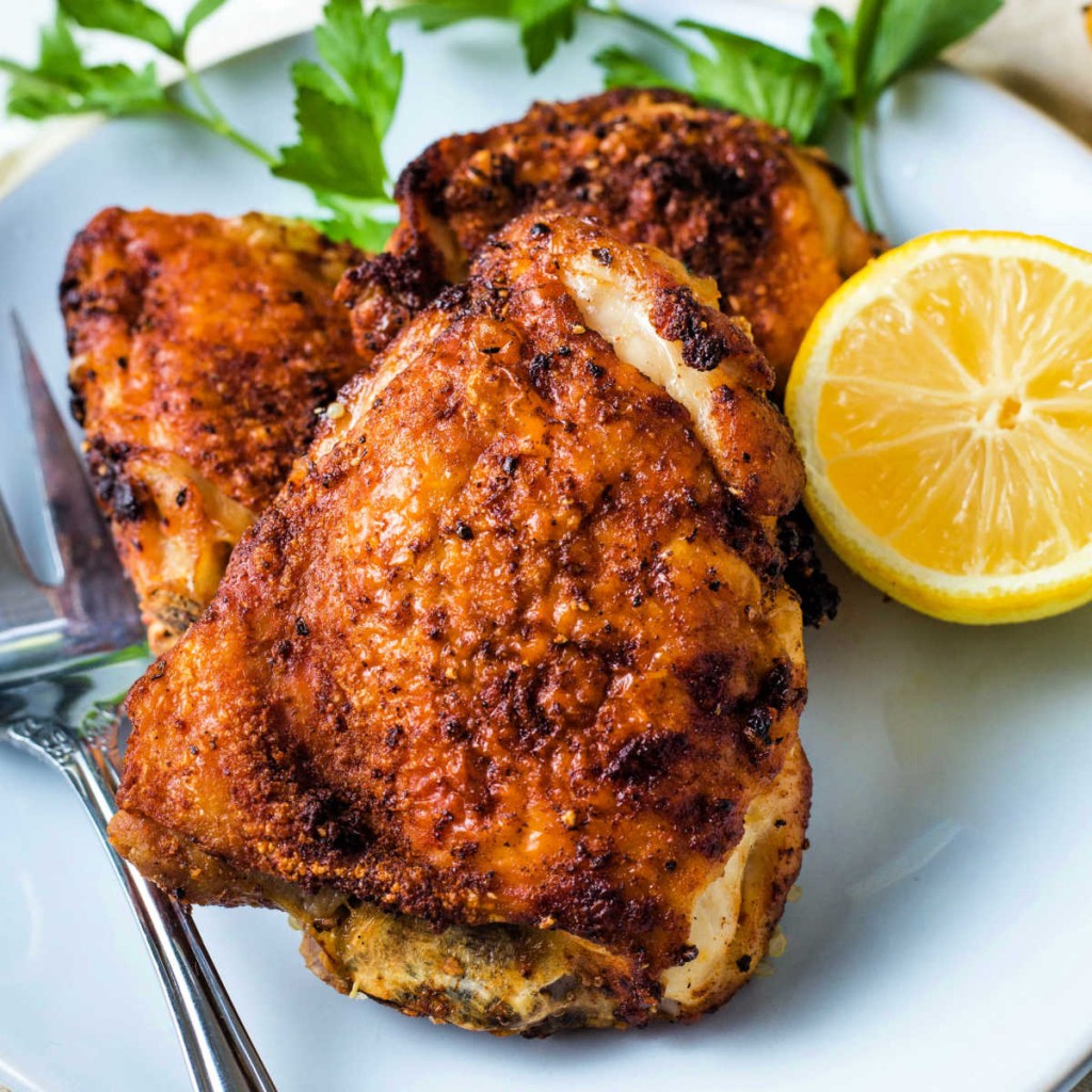a platter of air fryer chicken thighs with a lemon and parsley as a garnish.